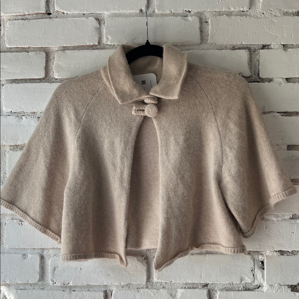 Cream cropped cape shrug cardigan in wool with button closure at neck.